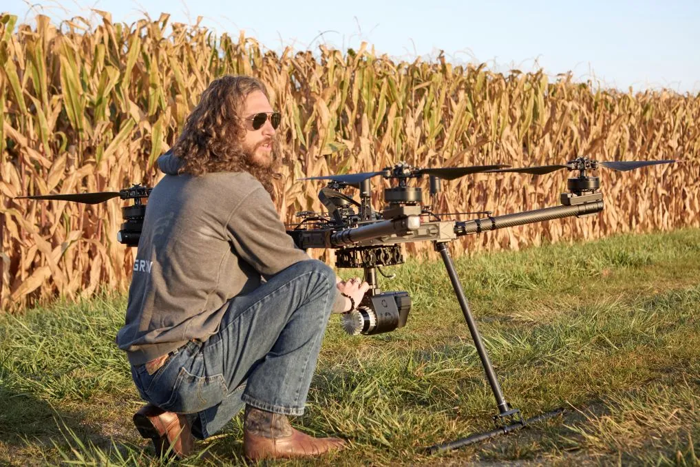 Person Kneeling By Drone Near Cornfield